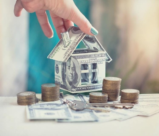 a hand holding a model house made from dollar bills
